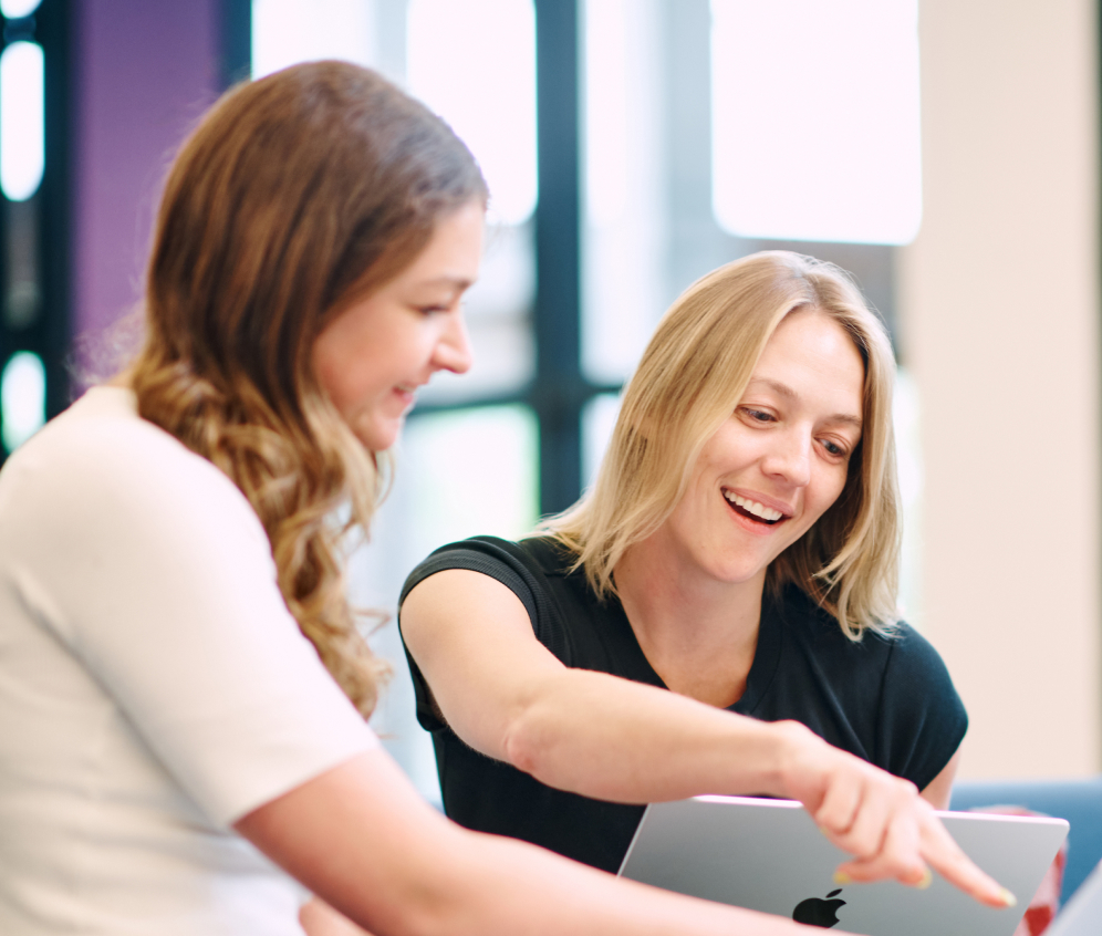 Photo of two women looking at and pointing at a laptop.